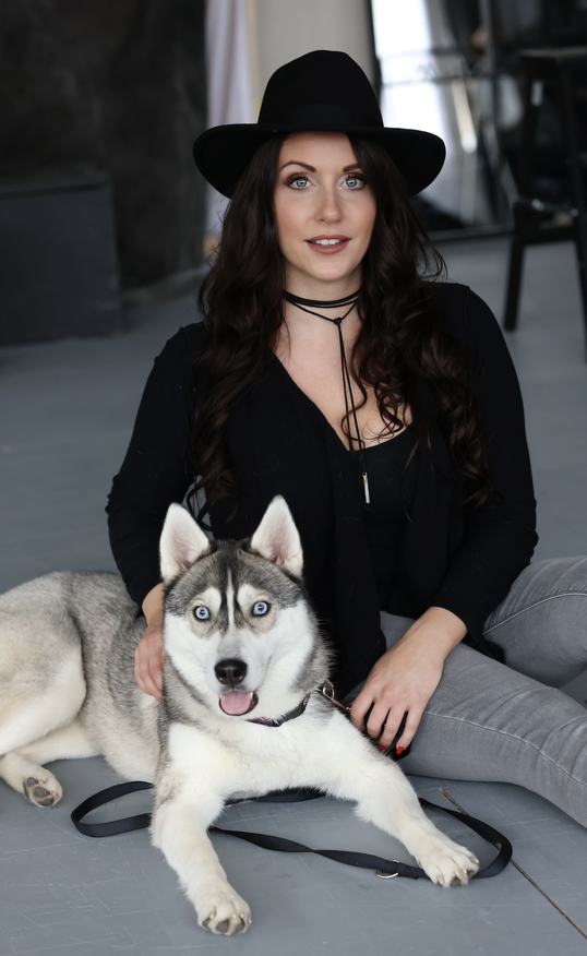 Aline Herger mit schwarzem Hut sitzt neben einem grau-weissen Husky