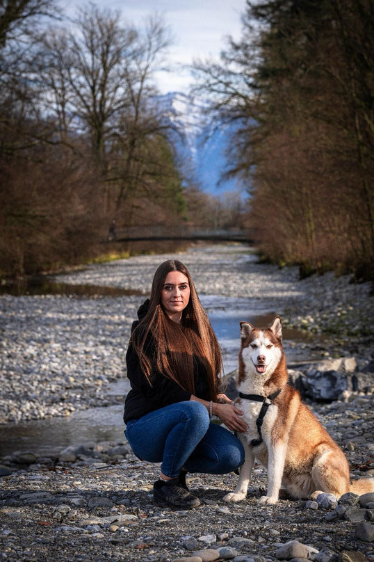 Fiona Freytag kniet an einem Fluss neben einem Husky